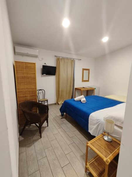 Habitación doble con cama azul, TV y aire acondicionado en Hotel Faraglione