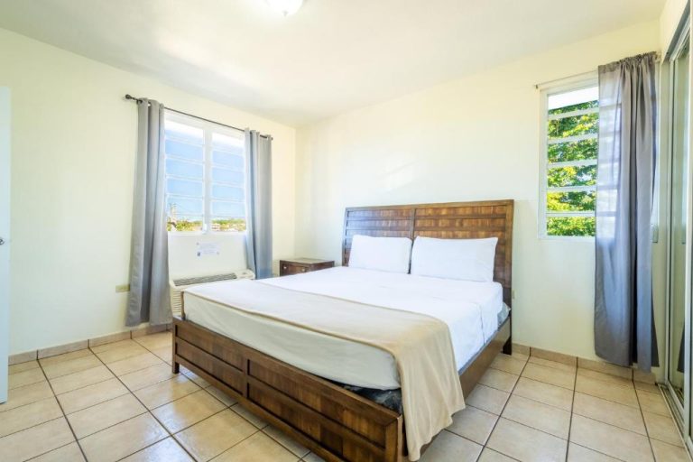 Habitación con cama doble y cabecero de madera en West Coast Apartments con ventanas y aire acondicionado