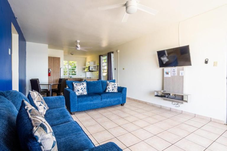 Sala de estar con sofás azules y TV de pared en West Coast Apartments, cocina al fondo