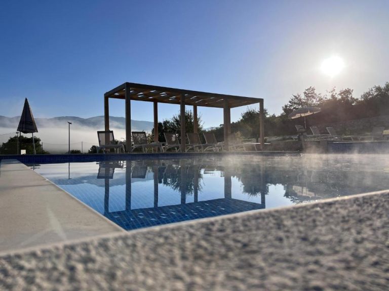 Piscina exterior con pérgola y tumbonas al amanecer en Plitvice Village con vistas a las montañas