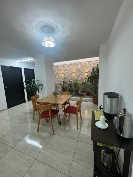 Salón comedor con mesa de madera y sillas rojas del Hotel Mar Inn Cali con zona de café
