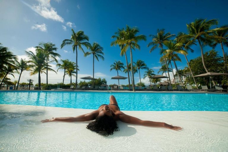 Mujer relajándose en la piscina exterior del Mahogany Hotel Residence & Spa rodeada de palmeras tropicales