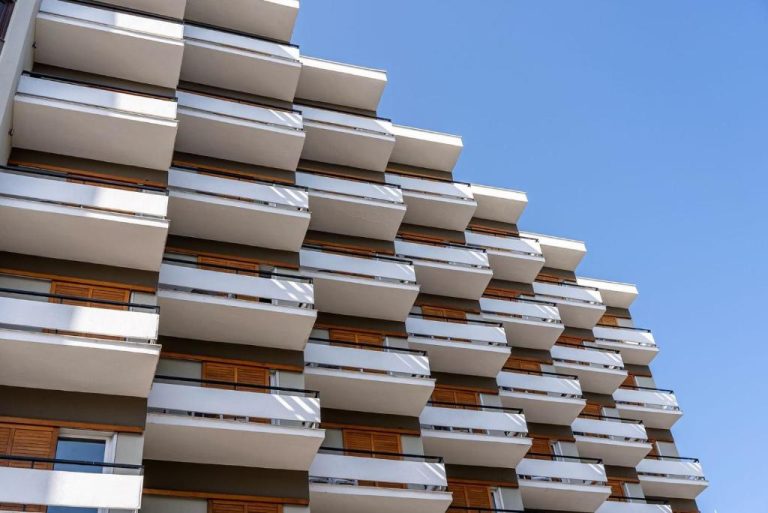 Fachada exterior del Oceanis Hotel con amplios balcones blancos y revestimiento de madera bajo cielo azul