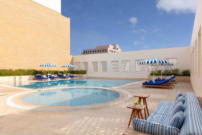 Piscina exterior con tumbonas azules y sombrillas del Al Najada Doha Hotel by Tivoli en Qatar