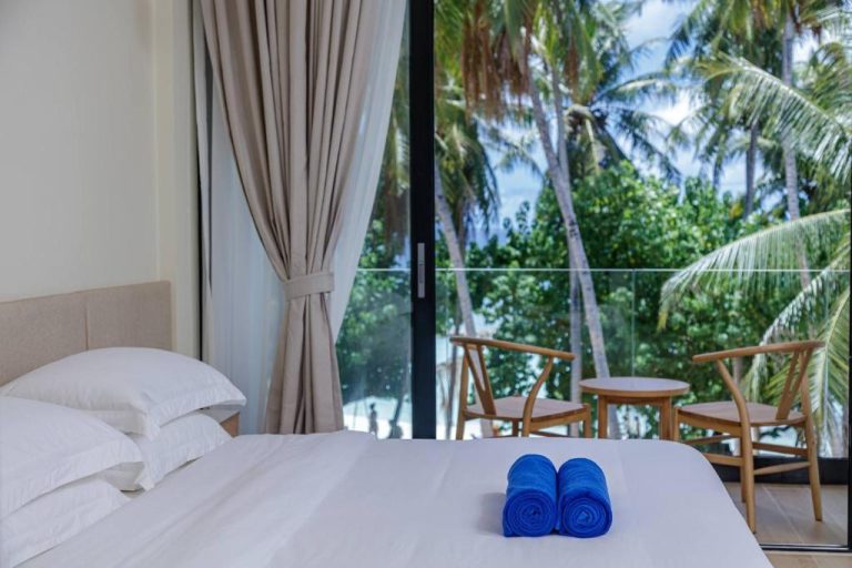 Habitación doble con cama blanca y vistas a palmeras tropicales en Kinan Boutique Hotel
