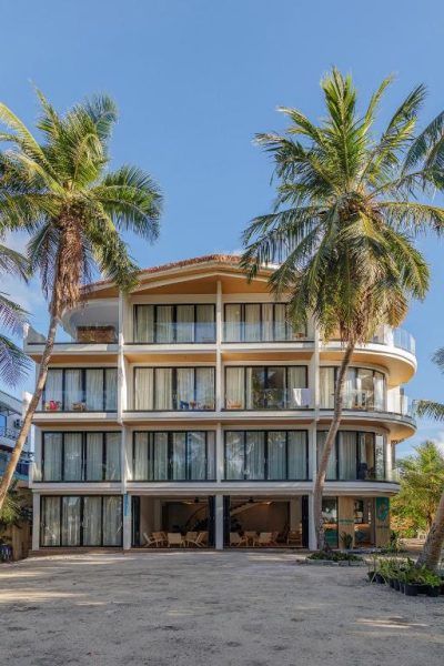 Fachada exterior del Kinan Boutique Hotel con palmeras tropicales y balcones frente a la playa