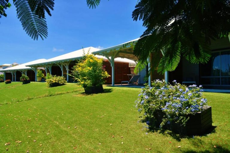 Jardín tropical con césped y flores del Hôtel Le Soleil Levant con terraza cubierta y vegetación exuberante