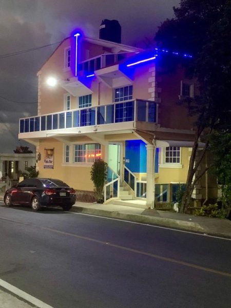 Fachada nocturna del Hotel Vista Sur con iluminación de neón azul y terraza en el segundo piso