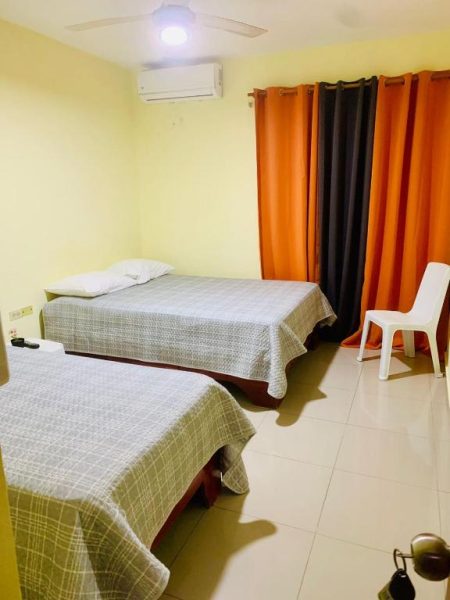 Habitación doble con dos camas, aire acondicionado y cortinas naranja en Hotel Vista Sur