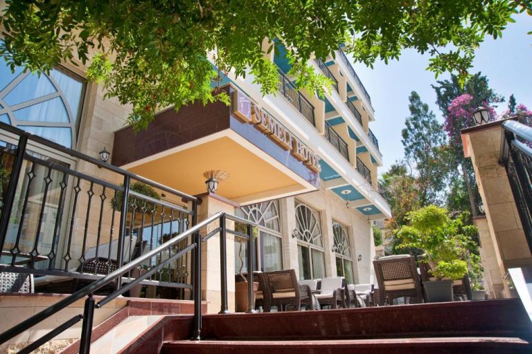 Fachada exterior y terraza con mesas del Semeli Hotel rodeada de vegetación mediterránea