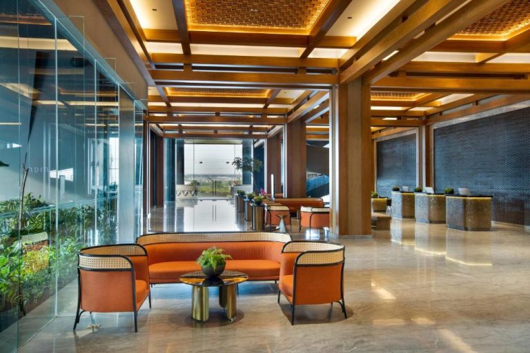 Elegante lobby del hotel Morazen Yogyakarta con sofás naranjas, techo de madera iluminado y recepción moderna