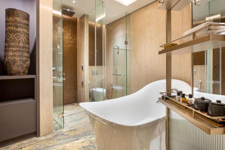 Baño de lujo con bañera exenta blanca y ducha de mosaico dorado en el hotel Morazen Yogyakarta