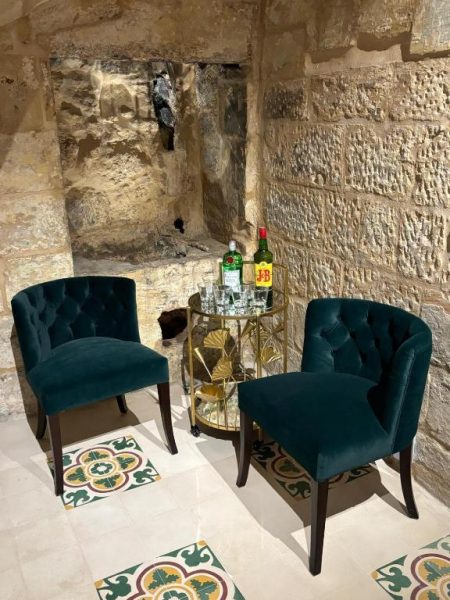 Salón íntimo con sillones de terciopelo verde y carrito de bebidas en Battery House Malta