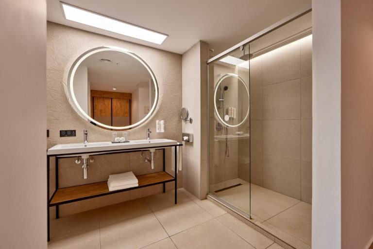 Baño moderno con ducha de cristal y lavabo doble con espejo redondo iluminado en Riu Palace Mauritius