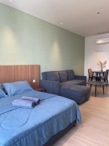 Habitación estudio con cama doble azul y sofá en Getawayhub Roxy Sematan Beach Apartment