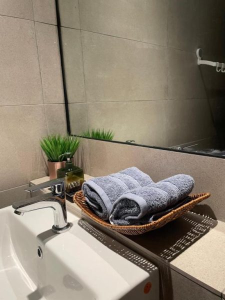 Baño moderno con lavabo, toallas grises y espejo en Getawayhub Roxy Sematan Beach Apartment