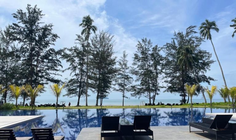 Piscina infinita con vistas al mar y palmeras en Getawayhub Roxy Sematan Beach Apartment