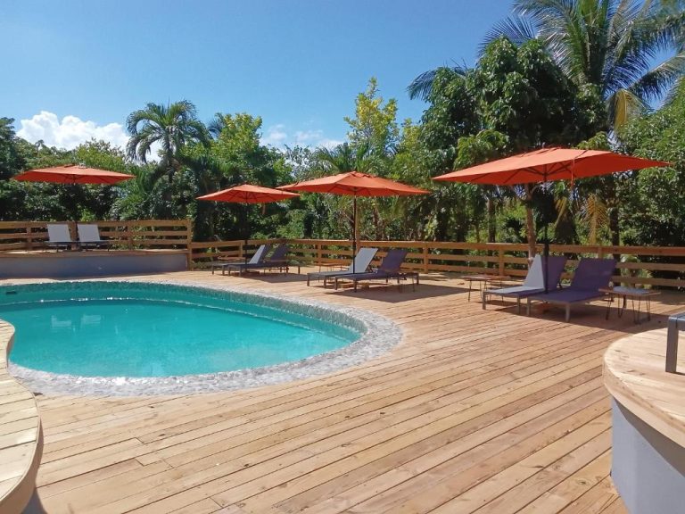 Piscina exterior con terraza de madera y tumbonas bajo sombrillas en LF Jungle Retreat