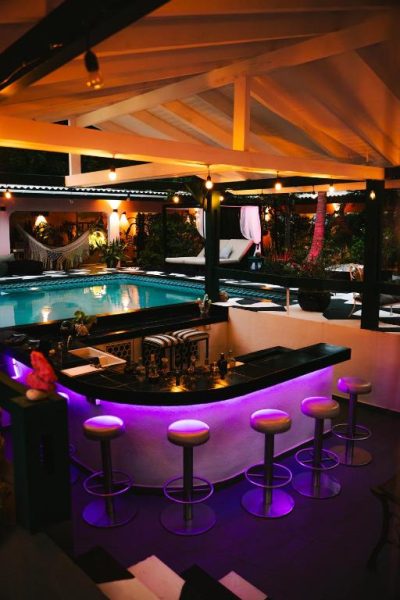 Bar con iluminación púrpura y taburetes junto a la piscina del Thuishaven Boutique Mini-Resort de noche