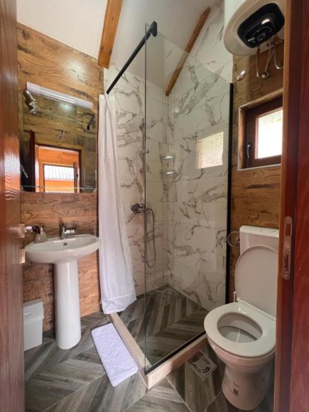 Baño con ducha de mármol, lavabo y paredes de madera rústica en Etno Selo Tačevine