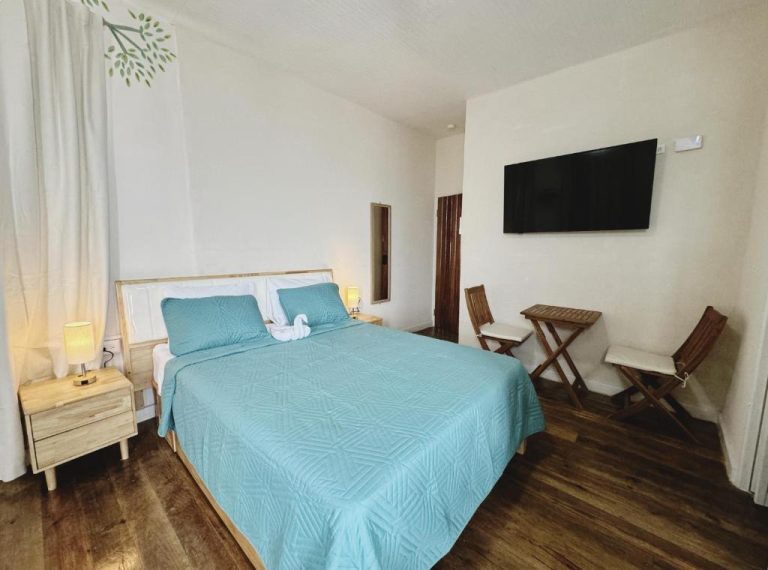 Habitación doble con cama azul, TV de pared y suelo de madera en Hotel Eden On the Sea