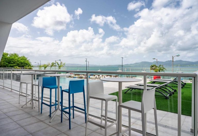 Terraza con sillas y mesas altas del B&B HOME Fort-de-France Marina con vistas a la piscina y al mar