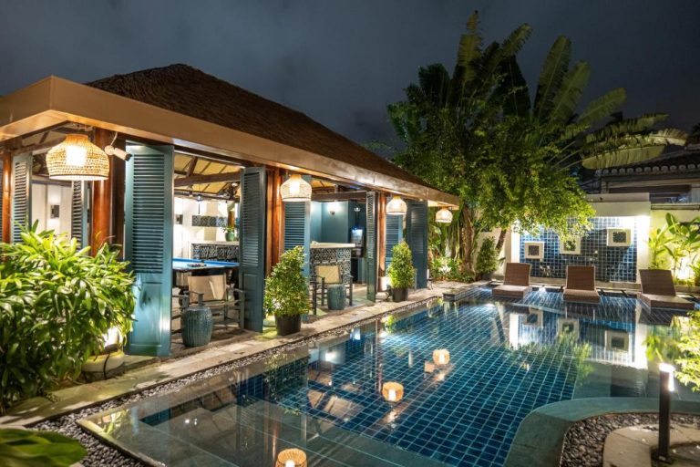 Piscina exterior iluminada de noche con zona de relax y bar en Maison Vy Hotel Hội An