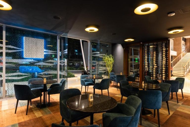 Bar lounge elegante con sillones azules y bodega de vinos en Hotel Estelar Milla de Oro
