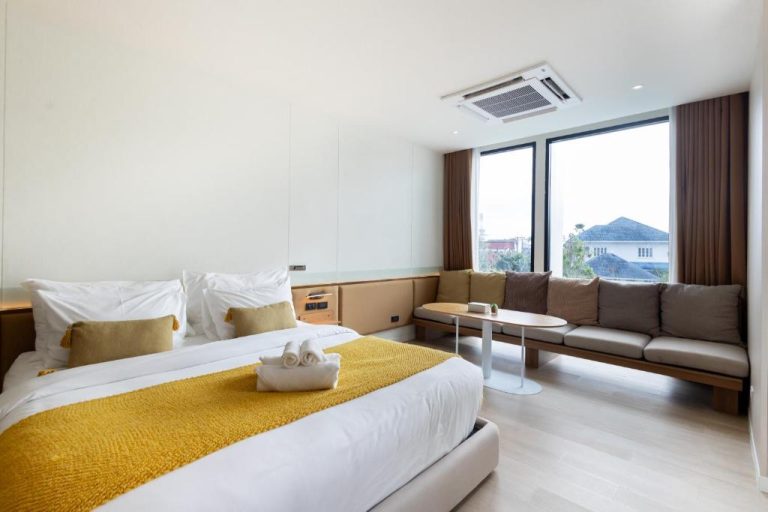 Habitación doble moderna con sofá y ventanal en Good Nakhonsawan Hotel, decoración en tonos dorados