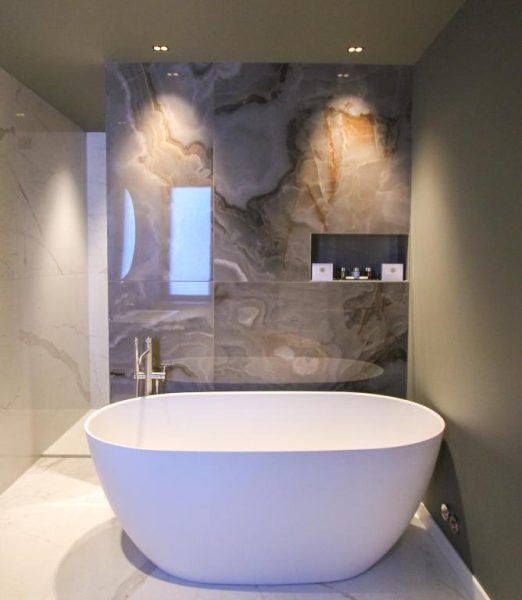 Bañera exenta blanca con revestimiento de mármol y ónix en el baño del Ambassador Palace Hotel