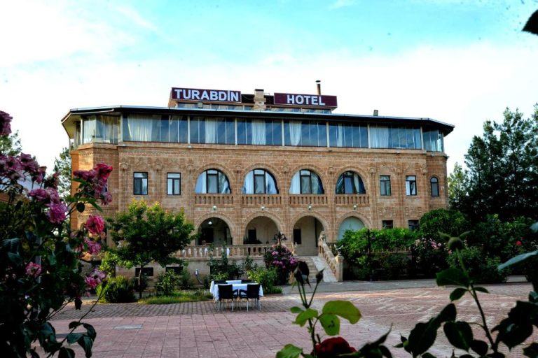 Fachada exterior del Turabdin Hotel con jardines floridos y arquitectura de piedra tradicional
