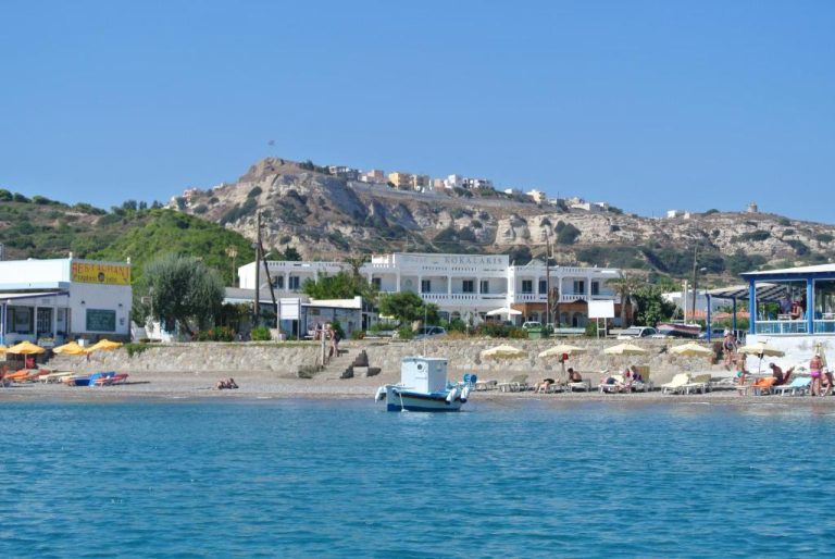 Vista desde el mar del Hotel Kokalakis con playa y colina rocosa al fondo en Grecia