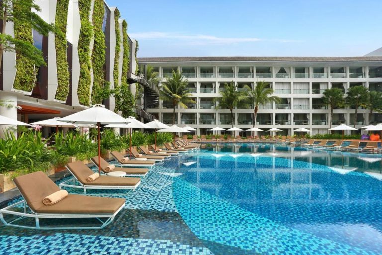 Piscina exterior con tumbonas y jardín vertical del The Stones Hotel Legian Bali