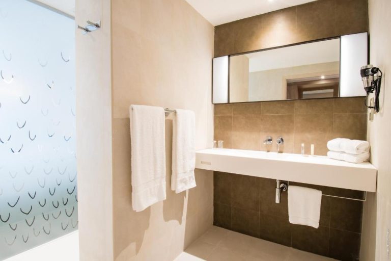 Baño moderno con lavabo empotrado, espejo amplio y toallas blancas en Simon Hotel