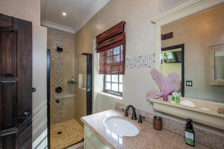 Baño con ducha de mosaico, lavabo sobre encimera de granito y ventana con persiana en The Pilot House