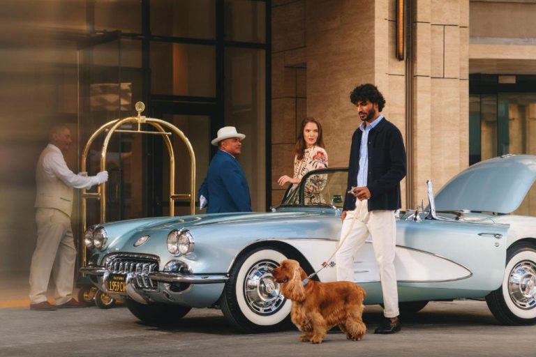 Llegada de huéspedes con perro al Regent Santa Monica Beach junto a un Corvette clásico azul de 1959