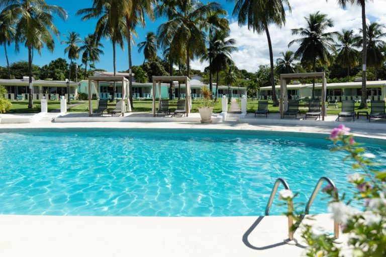 Piscina exterior cristalina con tumbonas y palmeras tropicales del All Seasons Resort