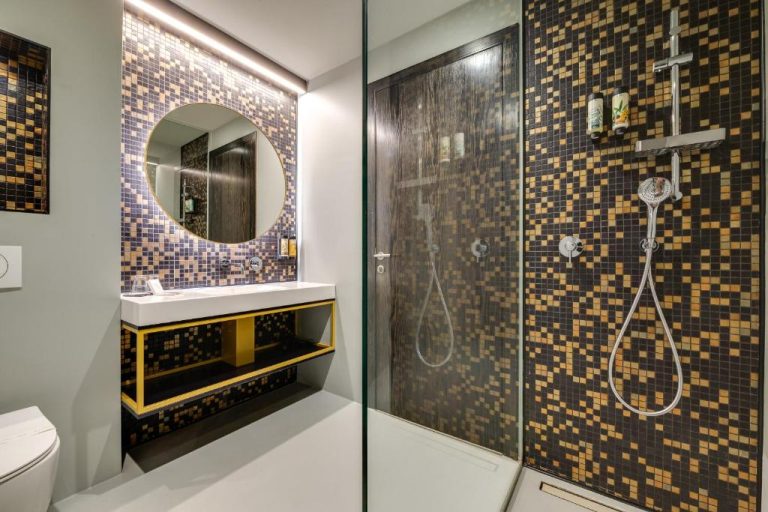 Baño moderno con ducha y mosaicos dorados y negros en el Lyra Hotel Plitvice