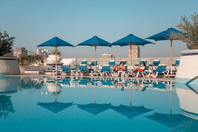 Piscina exterior con sombrillas azules y tumbonas del Hilton Cairo Grand Nile con vistas a la ciudad