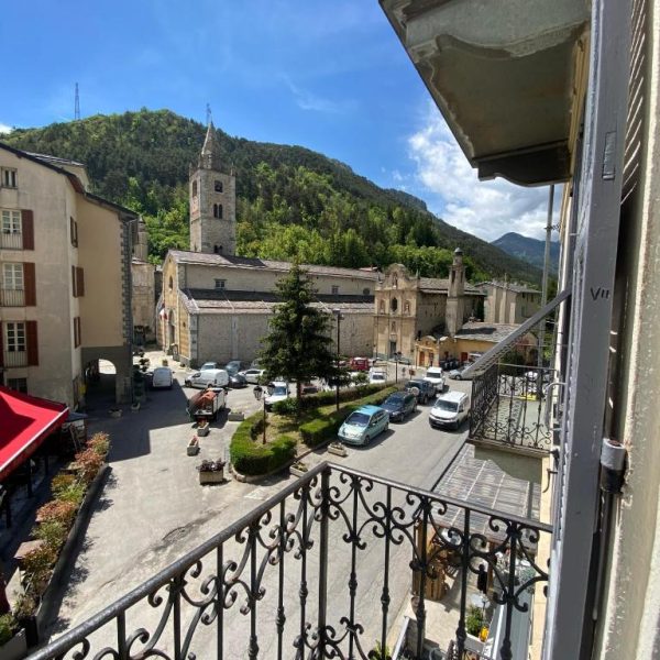 Vista desde el balcón del Hôtel Fleur des Alpes con plaza, iglesia histórica y montañas alpinas al fondo