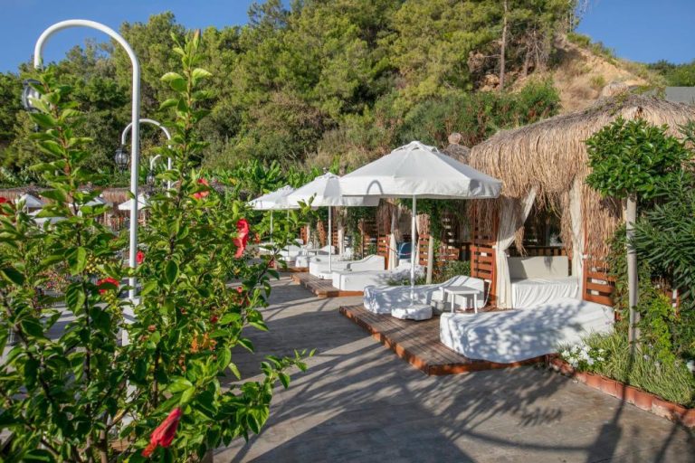 Zona de relax exterior con tumbonas blancas y sombrillas en Mylome Luxury Hotel & Resort rodeada de vegetación