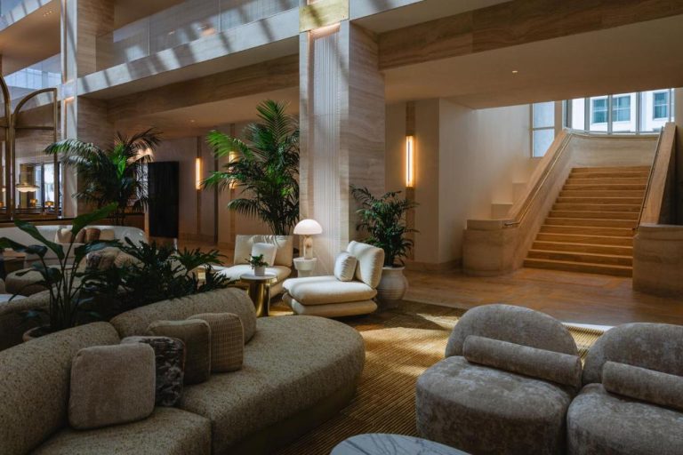 Elegante lobby del Regent Santa Monica Beach by IHG con sofás blancos, plantas tropicales y escalinata de mármol