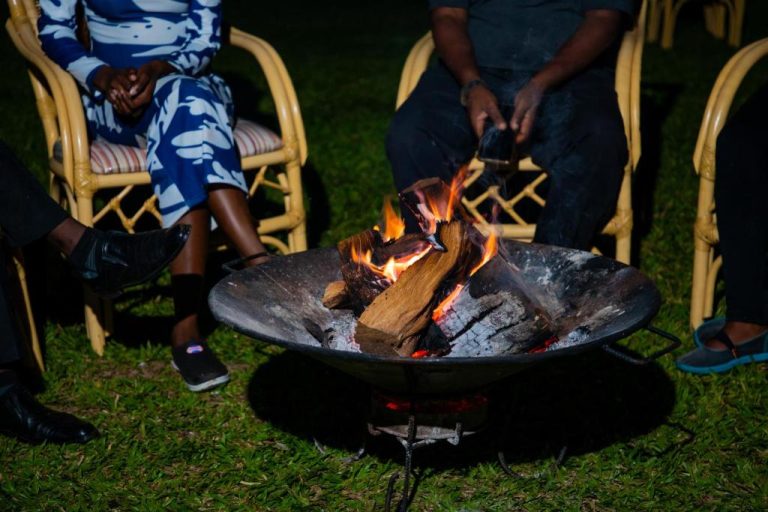 Fogata al aire libre con huéspedes reunidos en el jardín nocturno del Kisimani Eco Resort & Spa