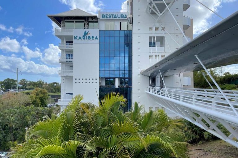 Fachada exterior del Hotel Karibea La Valmenière con pasarela blanca y vegetación tropical