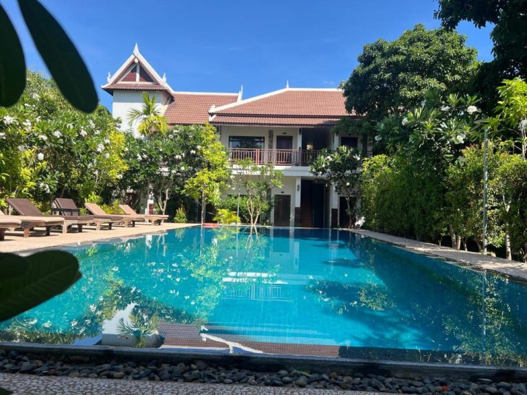 Piscina exterior rodeada de jardín tropical con tumbonas en Villa Phum Khnar, Camboya