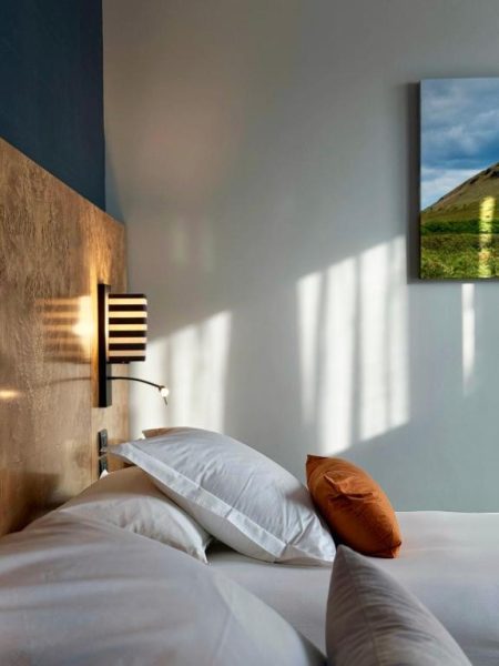 Habitación con cama doble y almohadas en Debaines Hotel Santiago con iluminación ambiental