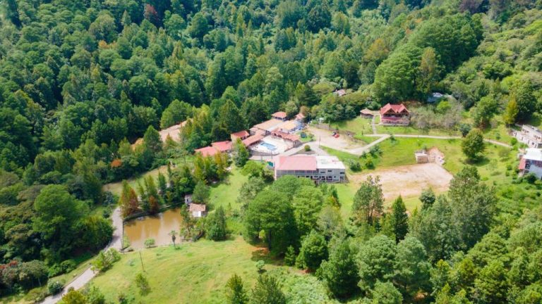 Vista aérea del Hotel y Cabañas ROS rodeado de bosque nativo con laguna y piscina exterior