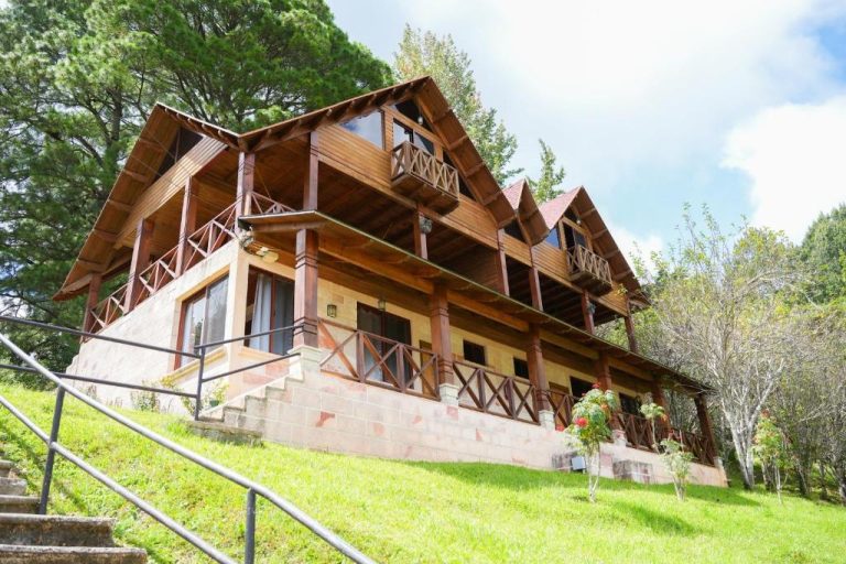 Fachada exterior de madera del Hotel y Cabañas ROS con balcones y jardín verde en la ladera