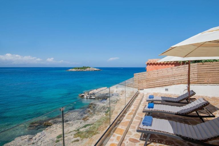 Terraza con tumbonas y sombrilla junto al mar cristalino en Kokkinos Studios With Pool & Sea View by ZanteWize