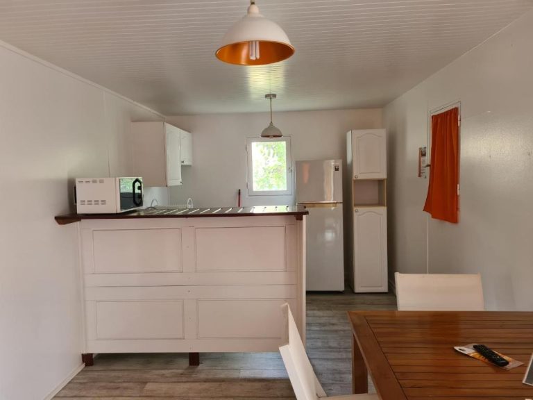 Cocina equipada con microondas y zona de comedor con mesa de madera en Hôtel Le Soleil Levant